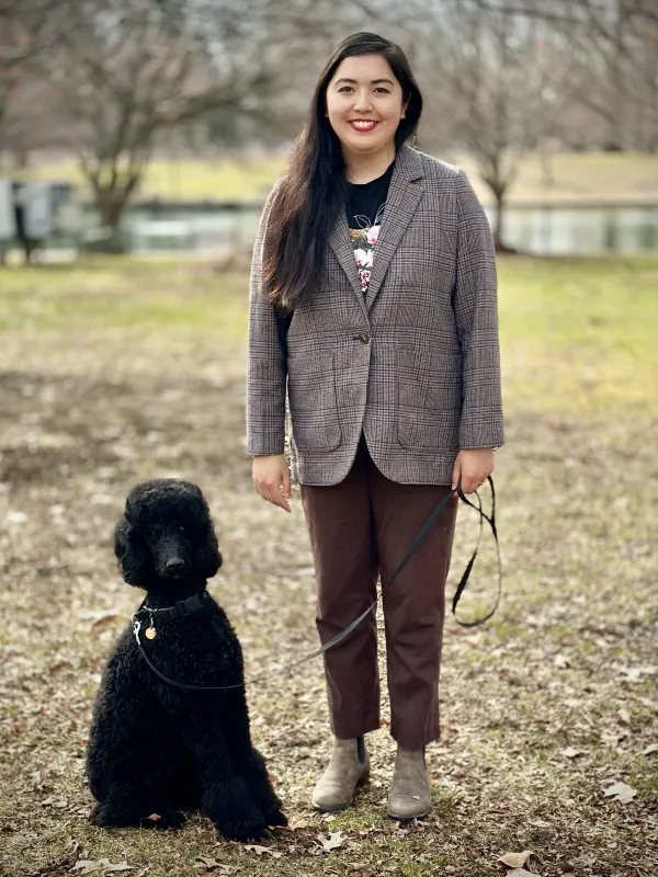Maya is standing, smiling next to her dog Rosalie who is a black standard poodle